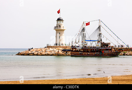 Una Crociera Turistica battello passa il faro all'entrata del porto, Alanya, Turchia Foto Stock