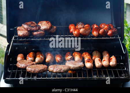 Salsicce e hamburger di essere cucinati su un barbecue Foto Stock