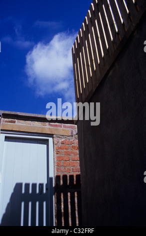 Picket Fence sulla sommità del muro alto getto ombra sulla parete inferiore e porta con puffy white cumulus cloud fa capolino dal cielo blu Foto Stock