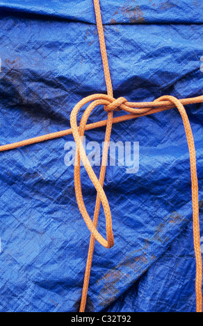 Dettaglio del profondo blu in plastica e biancheria telone di copertura oggetto di grandi dimensioni e legato con annodati in modo lasco corda arancione Foto Stock