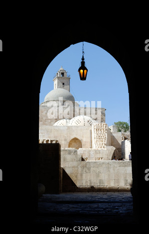 Ornato lanterna pende all'interno arcuato ingresso alla Cittadella con il minareto della grande moschea visibile. Aleppo. La Siria. Foto Stock