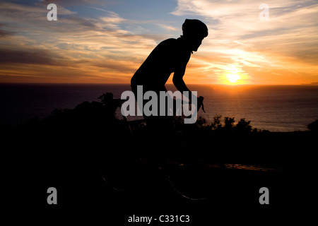 Un ciclista guarda il sole al tramonto mentre in sella alla sua moto Deer Creek Road in Malibu, California. Silhouette. Foto Stock