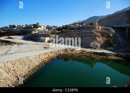 Oman, Wadi Fusc, vecchie case sulla scogliera rocciosa dalla montagna con piscina verde in primo piano Foto Stock