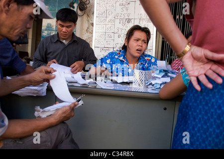 Gli uomini sono riuniti attorno a una donna la vendita di biglietti della lotteria su una strada di città in Phnom Penh Cambogia. Foto Stock