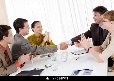 Foto di business di successo di handshaking partner dopo l'urto contro un ottimo affare con applaudire i dipendenti nelle vicinanze Foto Stock