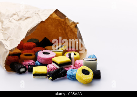 Liquirizia allsorts fuoriusciti da un sacchetto di carta. Grigio chiaro dello sfondo. Foto Stock