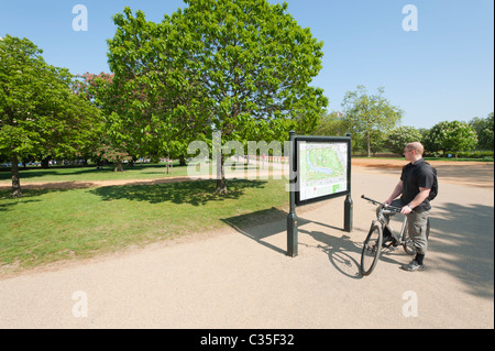 Cyclyst esaminando una mappa su un avviso pubblico pensione in Hyde Park di Londra, Inghilterra. Foto Stock