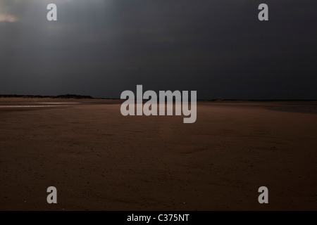 Un raggio di sole fa capolino tra le nuvole a North Norfolk beach Foto Stock