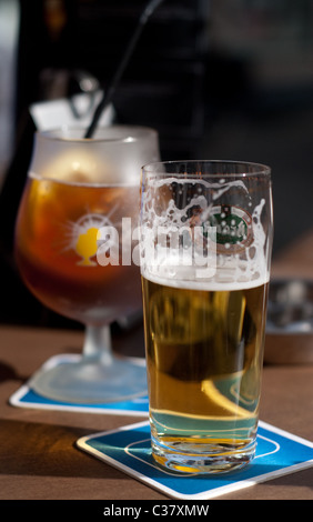 Un bicchiere di birra e un bicchiere di tè freddo permanente sulla birra stuoie su un tavolo del bar Foto Stock
