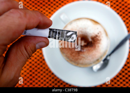 Un uomo versando Fairtrade zucchero nel suo cappuccino a Londra Foto Stock