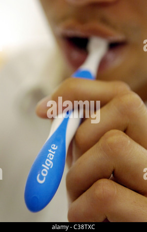 Un uomo con un spazzolino Colgate a pulire i suoi denti. Foto Stock