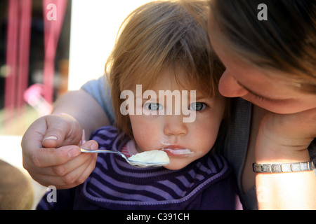 Il Toddler essendo alimentato yogurt da sua madre Foto Stock