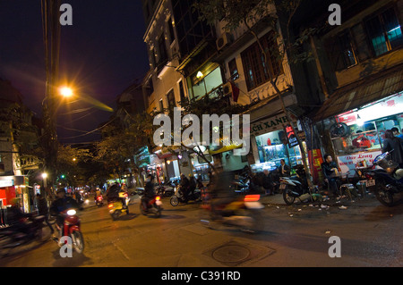 Notte orizzontale in prospettiva di una tipica streetscene del vecchio quartiere di Hanoi, con negozi aperti per il business e ciclomotori passato di guida Foto Stock
