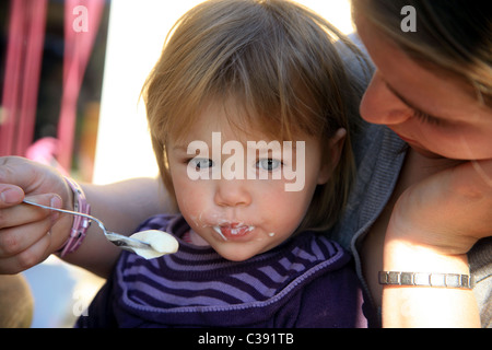 Il Toddler essendo alimentato yogurt da sua madre Foto Stock