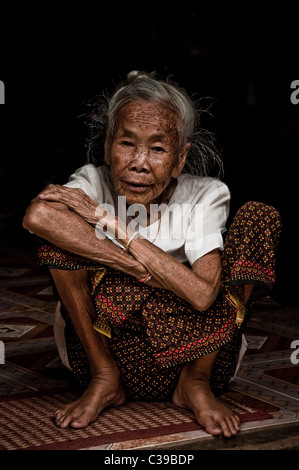 Donna anziana siede sul suo haunches nella sua casa sul fiume Mekong, Laos Foto Stock