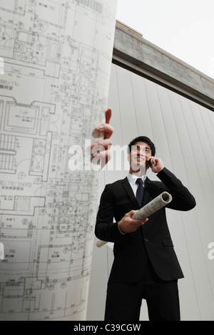 Donna che mantiene i progetti di un edificio mentre l uomo parla al telefono Foto Stock