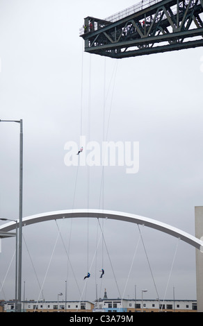 Tre persone completano una carità calata dall'Finnieston gru, Glasgow, nella parte anteriore del Clyde Arc bridge. La Scozia, Regno Unito. Foto Stock