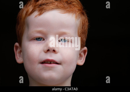 Un ragazzo di 7 anni la guarda. Sfondo nero. Sorridente Foto Stock