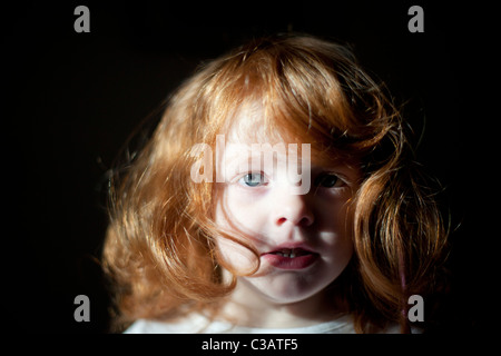 Ritratto di un anno quattro piccola vecchia ragazza con i capelli rossi su sfondo nero. Foto Stock