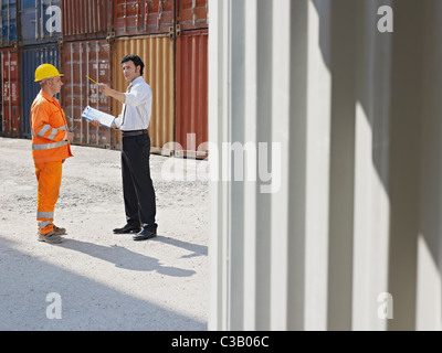 Adulto medio imprenditore e lavoratore manuale in piedi vicino ai contenitori di carico. Sagoma orizzontale, a piena lunghezza e spazio di copia Foto Stock