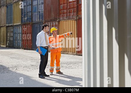 Adulto medio imprenditore e lavoratore manuale in piedi vicino ai contenitori di carico. Sagoma orizzontale, a piena lunghezza e spazio di copia Foto Stock