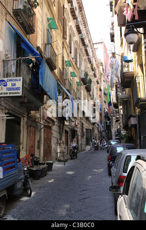 Una strada stretta a Napoli con lavaggio appeso all'asciutto e fiancheggiata da auto parcheggiate, Italia Foto Stock