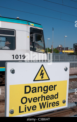 Pericolo cavi aerei sotto tensione segnale di avvertimento Mertolink con il tram che passa. Foto Stock
