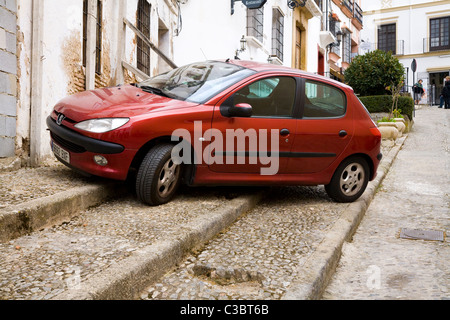 Una Peugeot 206 auto parcheggiate sul marciapiede in tipico spagnolo tradizionale strada di ciottoli / Street nella città bianca di Ronda, Spagna. Foto Stock