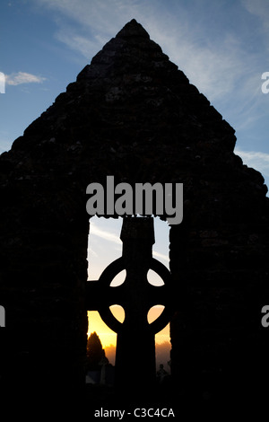 Croce celtica e tempio profilarsi all'alba, Monastero di Clonmacnoise, nella contea di Offaly, Irlanda. Foto Stock