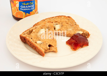 Una fetta di in parte imburrata mangiato pane tostato con un vasetto di marmellata di arance su un tavolo. Inghilterra Regno Unito Gran Bretagna Foto Stock