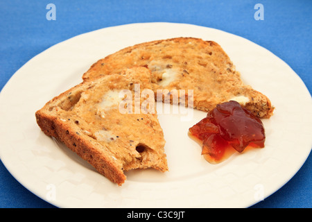 Una fetta di in parte imburrata mangiato pane integrale tostato e un blob di marmellata su una piastra. Regno Unito Foto Stock