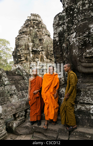 Tre monaci buddisti che sta sotto il gigante facce di Avalokitesvara presso il Bayon nel centro di Angkor Thom in Cambogia Foto Stock