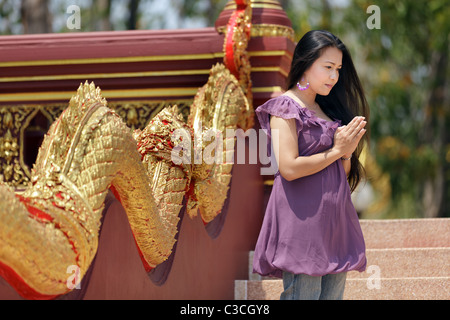 Giovane donna asiatica pregando buddha vicino tempio, Thailandia Foto Stock