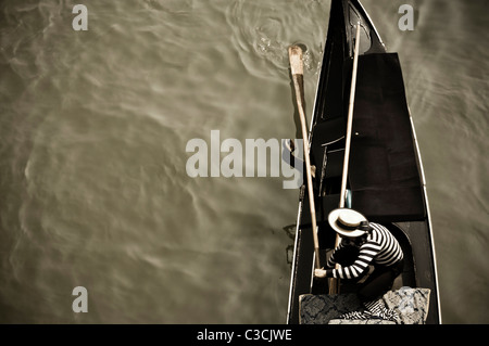 Un gondoliere il suo sterzo gondola in preparazione per la movimentazione sotto un ponte a Venezia, Italia. Foto Stock