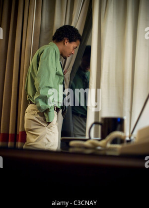 Un imprenditore si affaccia una finestra pensieroso mentre si lavora fino a tarda notte nella sua camera di albergo durante un viaggio di lavoro. Foto Stock