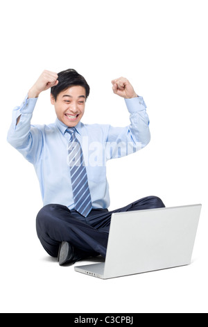 Un happy businessman seduto sul pavimento con il suo computer portatile Foto Stock