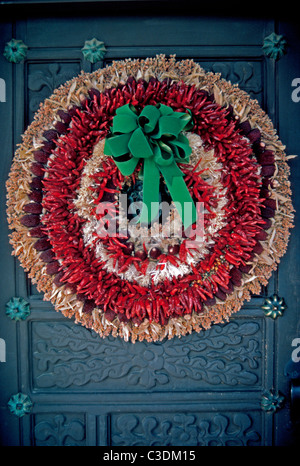 Un tradizionale Southwestern vacanze di Natale corona appeso su un vecchio legno scolpito le funzioni della porta essiccato peperoncino rosso in Santa Fe, New Mexico, negli Stati Uniti. Foto Stock