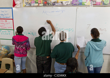 Gruppo di maschio e femmina gli studenti delle scuole medie di scrivere su una lavagna bianca all'interno di aula scolastica Foto Stock