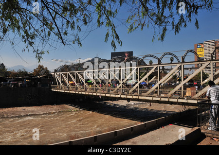 Blue sky view persone attraversando traliccio metallico ponte sul canale canalizzato Rio Mapocho verso il Mercado de Flores, Santiago del Cile Foto Stock