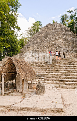 COBA rovine Maya, Messico - i turisti salire i 120 scalini del tempio struttura nota come la Iglesia (la chiesa). La piccola struttura con il tetto di paglia in primo piano è stata designata come Stela 11. Coba è un esteso sito maya sulla penisola dello Yucatan in Messico non lontano dalle più famose rovine di Tulum. Accoccolato tra due laghi, Coba è stimato essere stata la casa di almeno 50.000 residenti presso la sua pre-colombiano di picco. Foto Stock