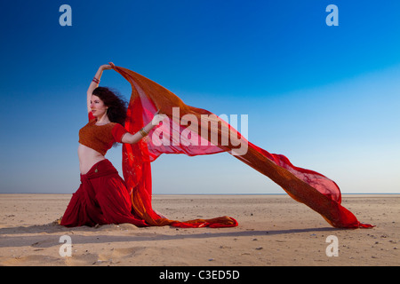 Giovane e bella "danzatrice del ventre' pongono gli scioperi contro il cielo drammatico e la spiaggia in abbigliamento indiano, UK. Bellydancer e yoga Foto Stock