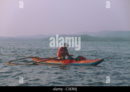 Pescatore in canoa outrigger tirando in reti Koggala Lake Sud Sri Lanka Foto Stock