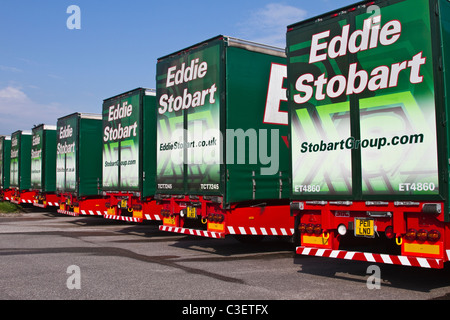 Fila di camion Eddie Stobart parcheggiati rimorchi e container al parcheggio camion. Fila di veicoli per il trasporto HGV AEC Scania 440 Livery. Foto Stock