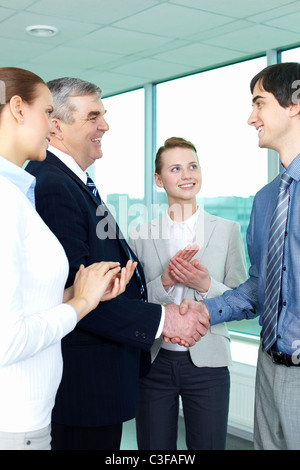 Foto di uomini d'affari di successo lo handshaking dopo la sorprendente trattare applaudire le donne nelle vicinanze Foto Stock