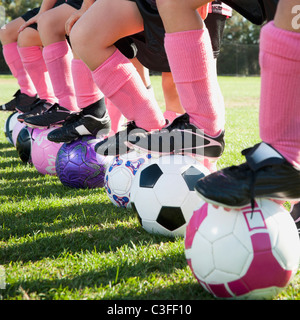 Ragazza i giocatori di calcio in piedi con i piedi su palloni da calcio Foto Stock