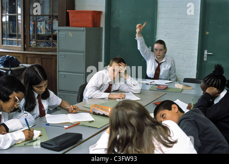 Scuola secondaria di scena in aula in uniforme con una ragazza alzando la mano per rispondere a una domanda Foto Stock