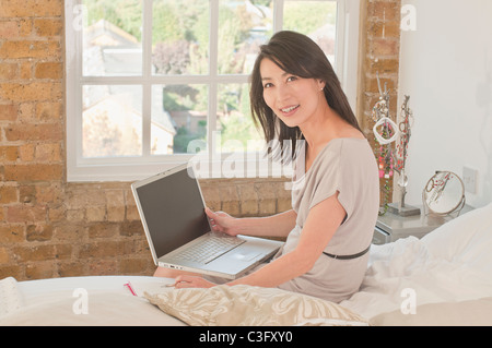 Il coreano donna seduta sul letto tramite computer portatile Foto Stock