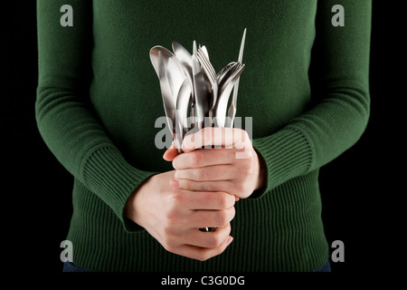 La donna in un ponticello verde contiene un mucchio di posate in mano Foto Stock
