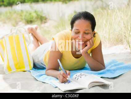 Nero donna facendo cruciverba sulla spiaggia Foto Stock