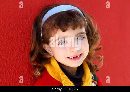 Sorridente bambina frastagliate denti frontali sorriso sul muro rosso sfondo Foto Stock